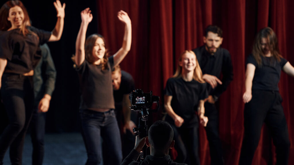 Nuoria iloisia ihmisiä teatteriharjoituksissa, joita valokuvataan.