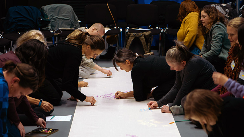 Ihmiset kirjoittelevat suurelle paperille, joka on lattialla. 