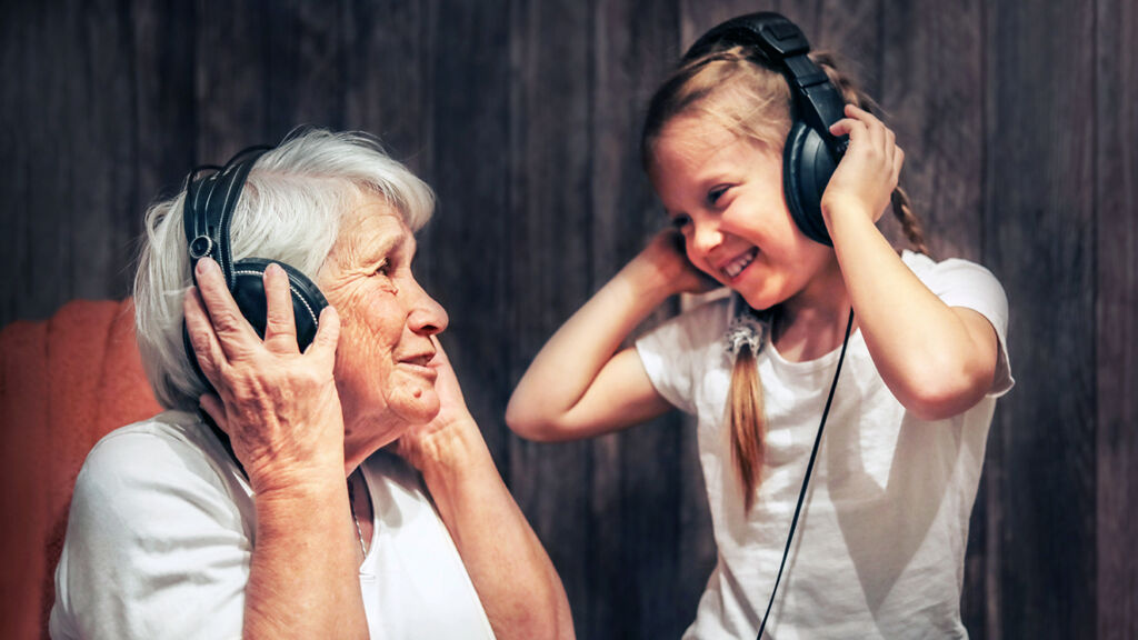 Vanha nainen ja tyttö kuuntelevat yhdessä kuulokkeilla musiikkia.