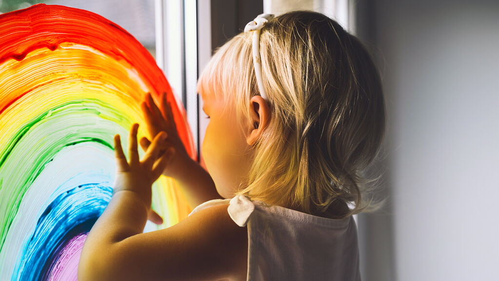 Lapsi katsoo ulos ikkunaan maalatun sateenkaaren läpi.